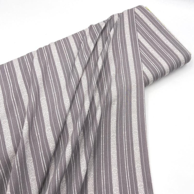 A bolt of grey and white striped fabric laying diagonally on a white table top. 