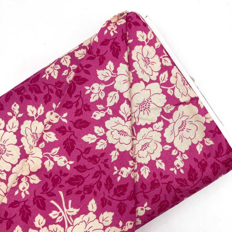 A bolt of quilting cotton with floral motifs in deep pink and ivory on a lighter pink background.