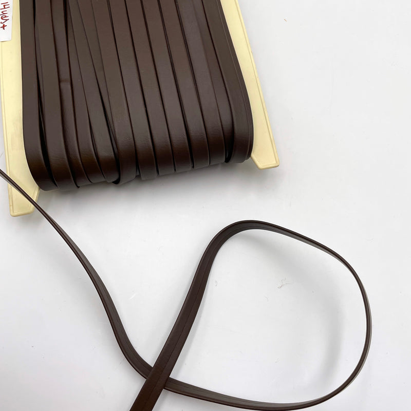 A bolt of dark brown faux leather trim laying on a white table.