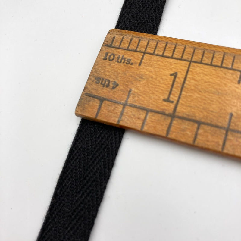 a close-up of black twill tape layign on a white table with a wooden ruler to show the width