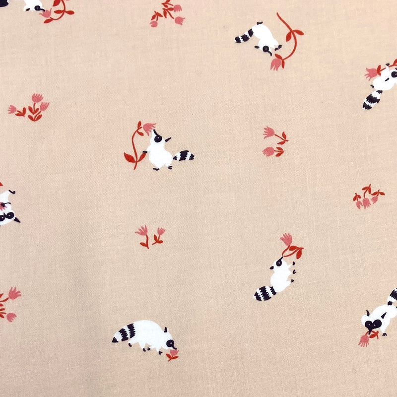 a peach fabric with small white raccoons sniffing pink flowers